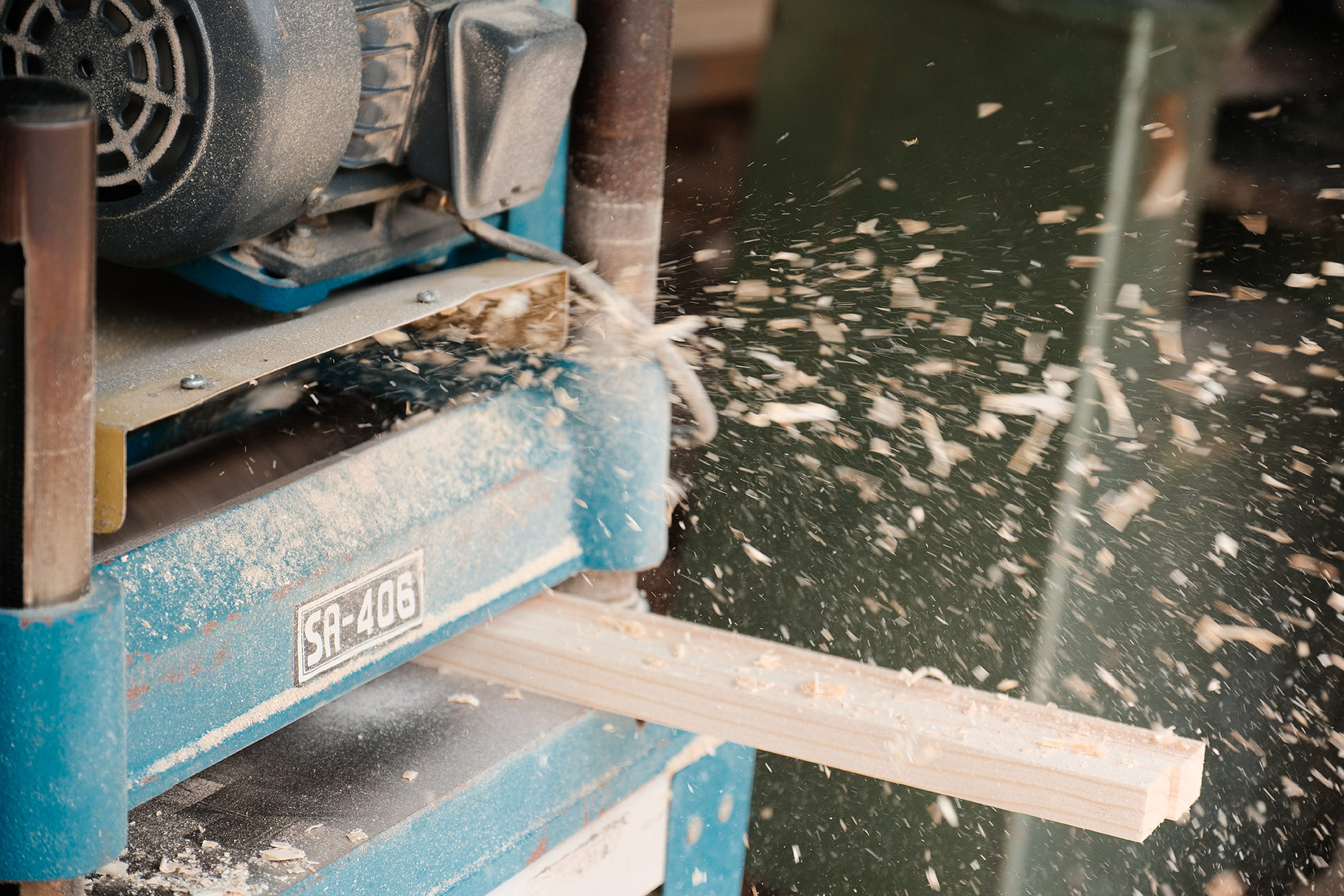 Rough lumber running through a moulder with sawdust flying